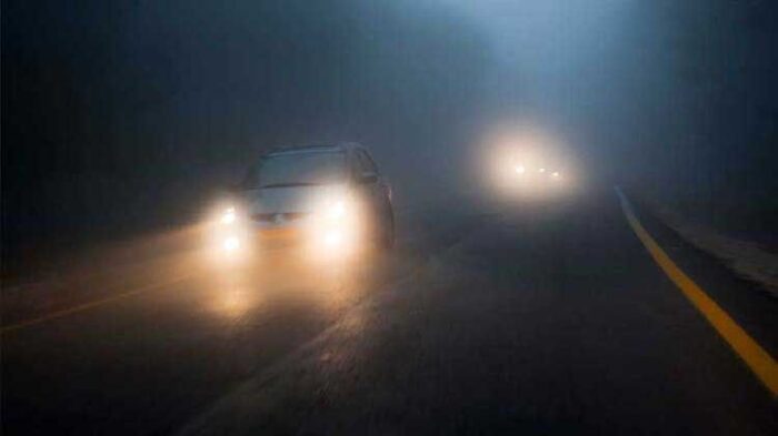 Auto’s met koplampen rijden bij zeer dichte mist op een donkere weg